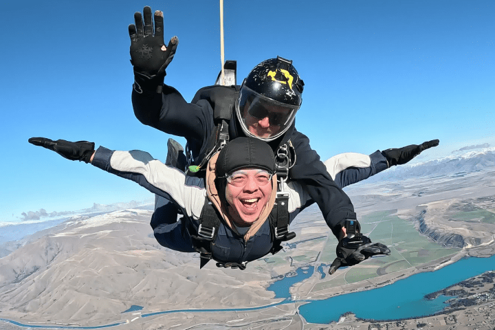 Two people tandem skydiving over a landscape with rivers and fields.