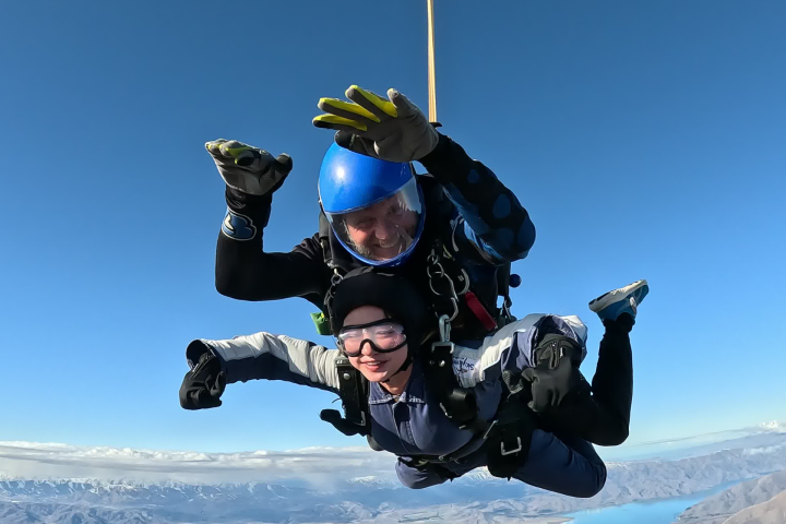 Two people skydiving with a clear blue sky and landscape below.