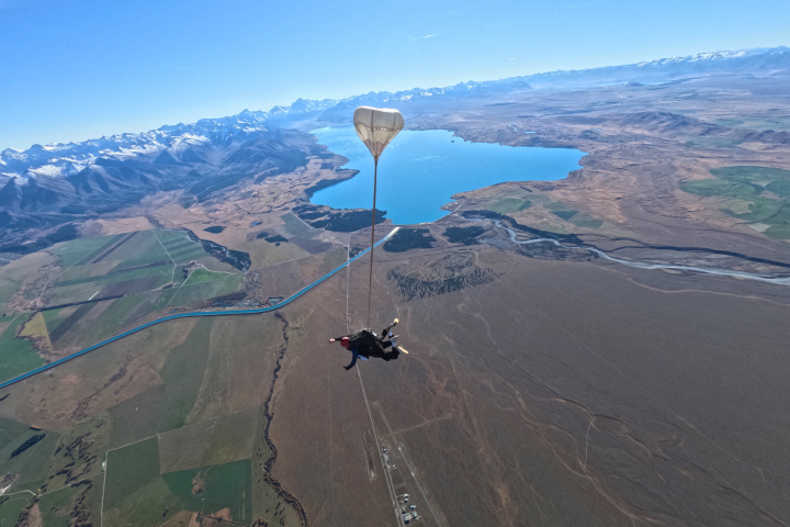 Skydiver with parachute over a vast landscape and a large lake.