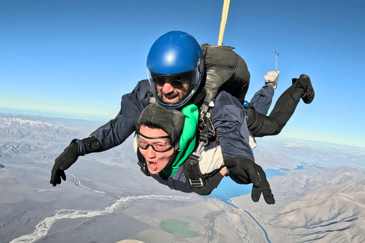 Two people tandem skydiving over a mountainous landscape.