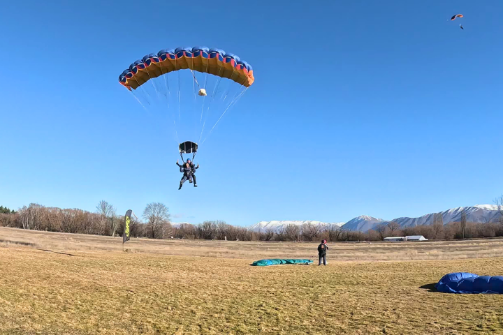 Parachutist landing in a grassy field with mountains in the background.