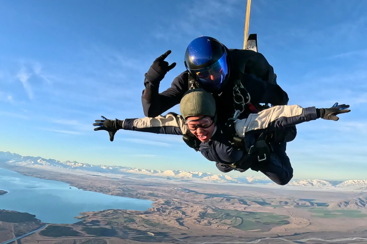 Two people skydiving over a landscape with mountains and a lake.