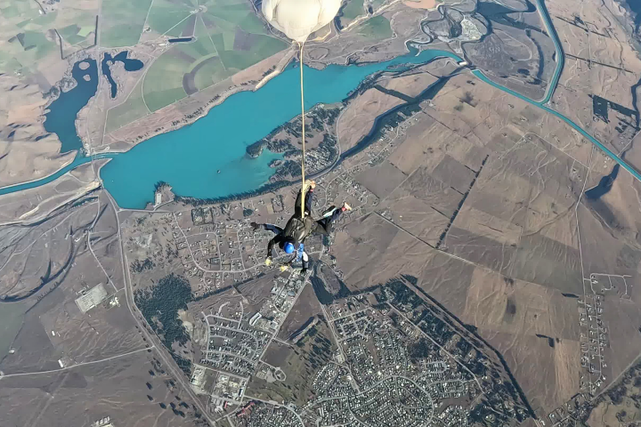 Skydiver descending with parachute over a landscape of fields and a river.