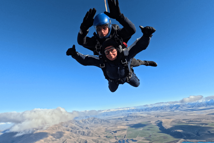 Two people tandem skydiving over scenic mountains and lake.