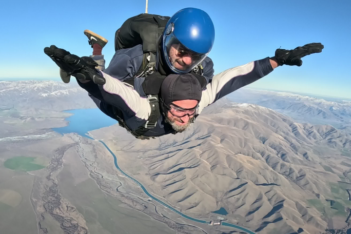 Tandem skydivers descending above mountainous landscape.