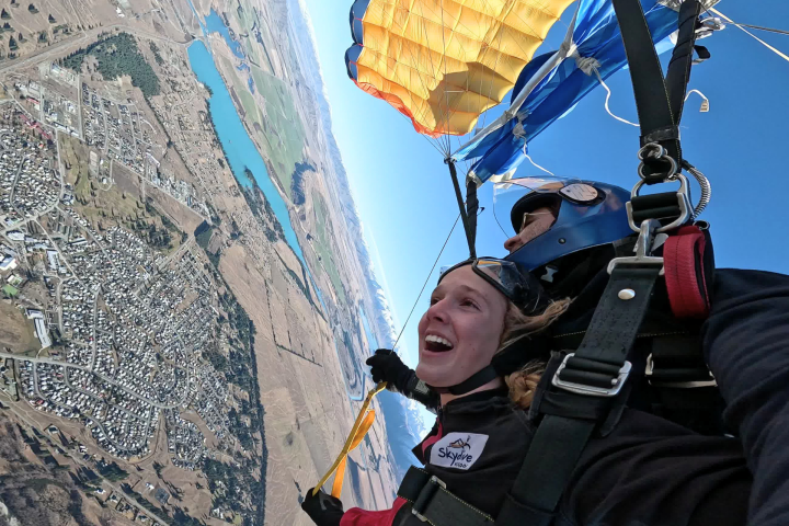 Skydiver tandem pair with parachute open, overlooking landscape and town.