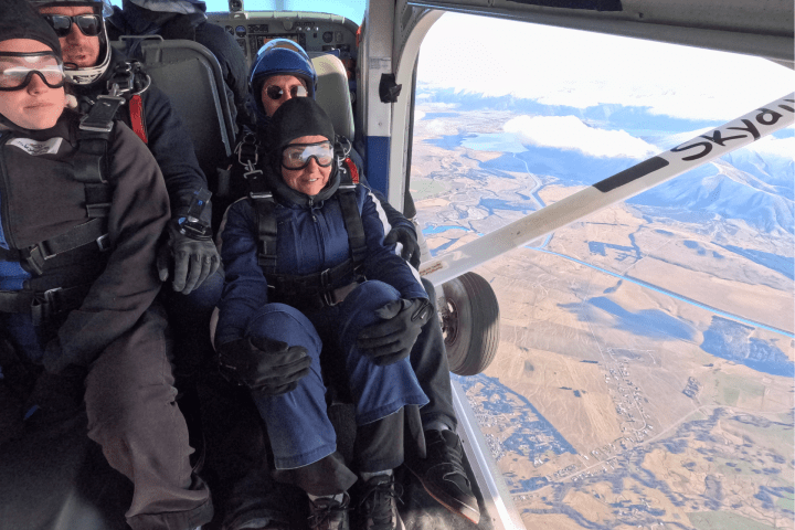 Group of four people in a plane preparing to skydive over a landscape.