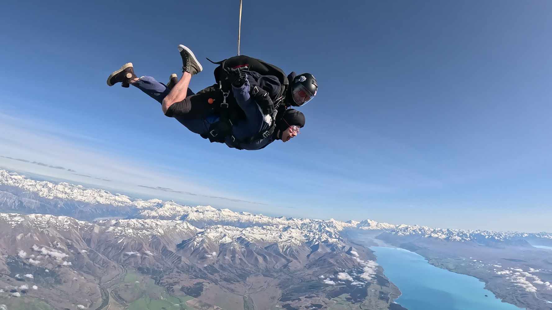 tandem skydivers jump over lake pukaki with snow capped mountains in the background