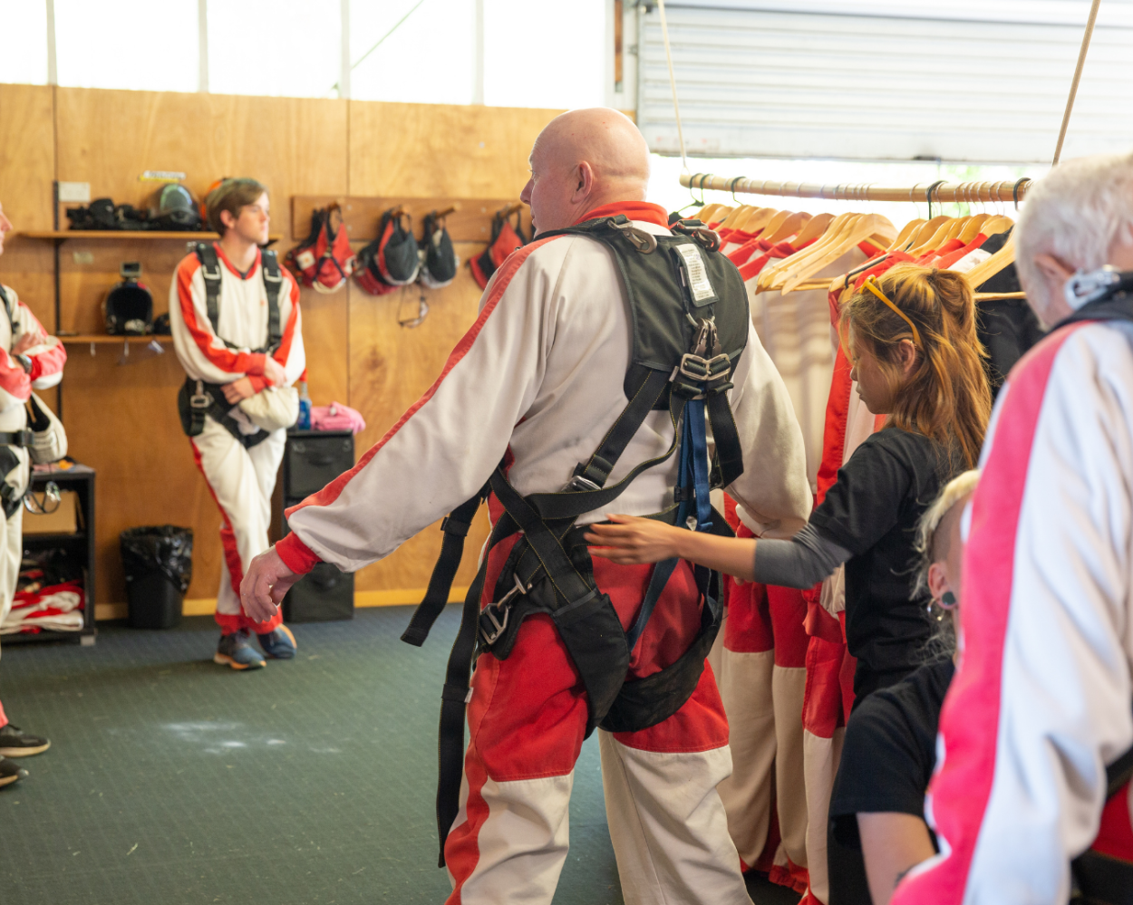 Skydivers in red and white suits preparing with harnesses in a training room.