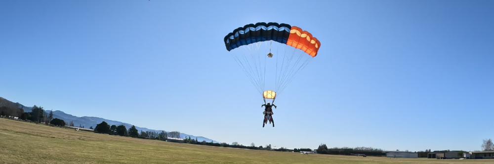 Tandem skydivers land with a colorful parachute on an open grassy field.