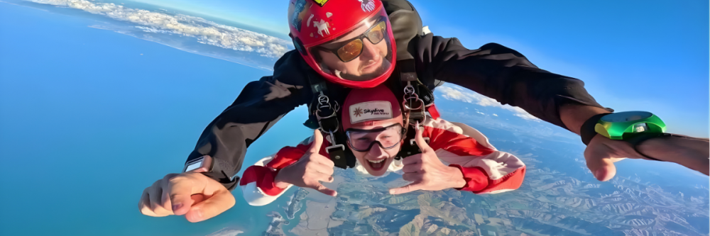 Two people tandem skydiving over a scenic landscape with ocean and clouds.