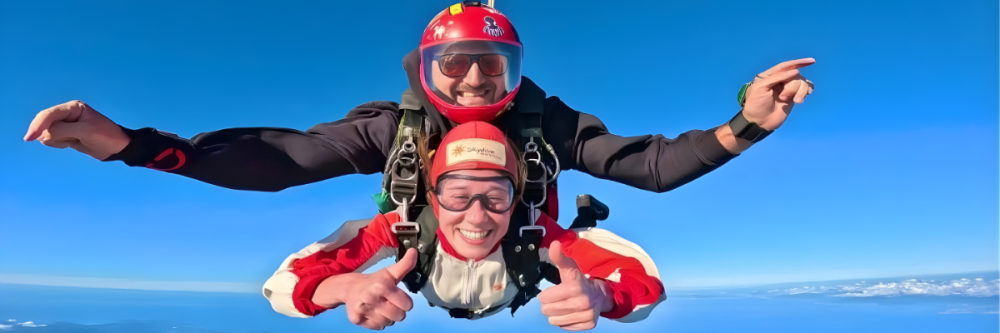 Two people tandem skydiving with a clear blue sky and distant clouds.