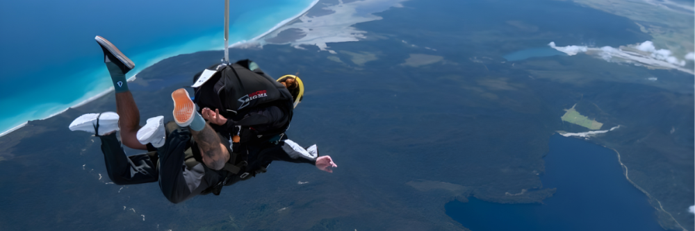Two people tandem skydiving over coastline and ocean.