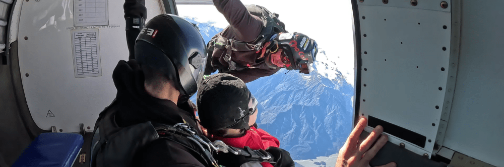 Skydivers preparing to jump from an airplane over mountains.
