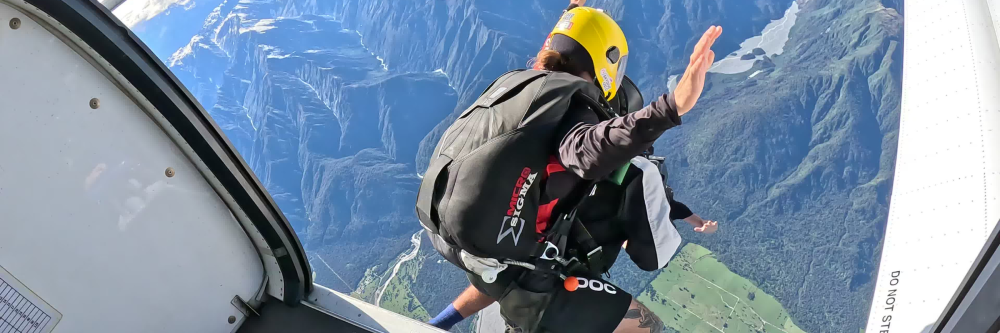 Skydiver in yellow helmet jumping from airplane over mountains.