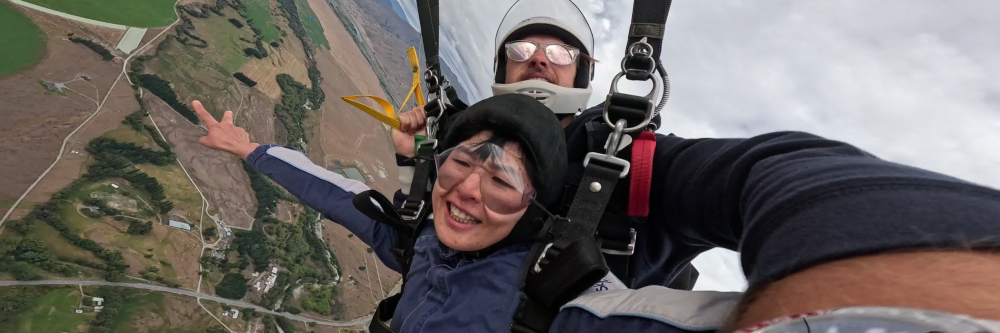 Two people tandem skydiving over a rural landscape.
