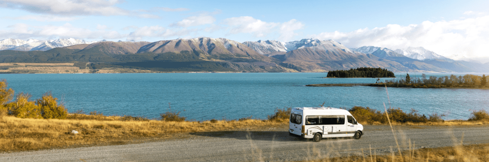 White camper van by lake with mountains in the background under a clear sky.