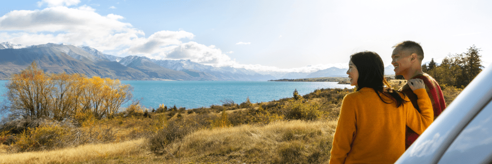Two people enjoy scenic view of lake and mountains, sunny day.