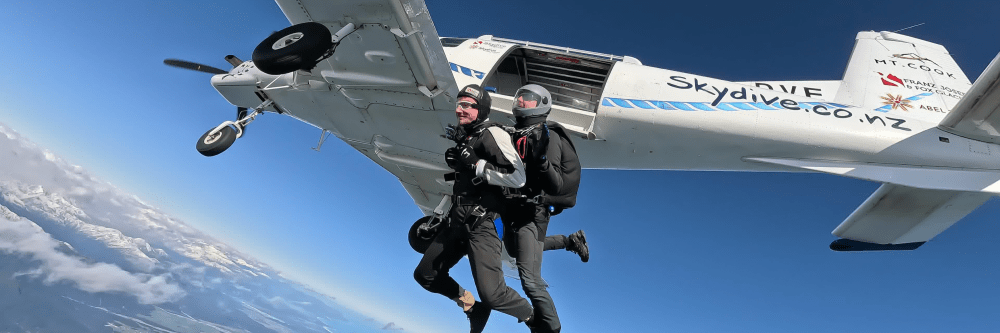 Two skydivers jumping from a plane into clear blue sky.