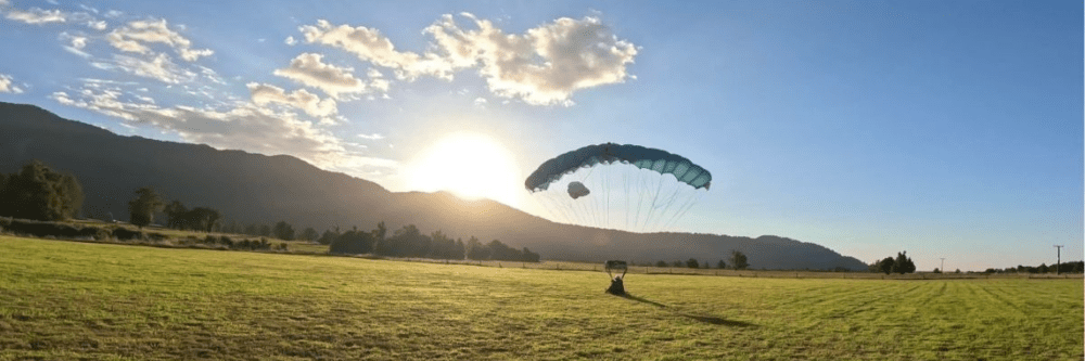 Person landing with a parachute on a grassy field at sunset.