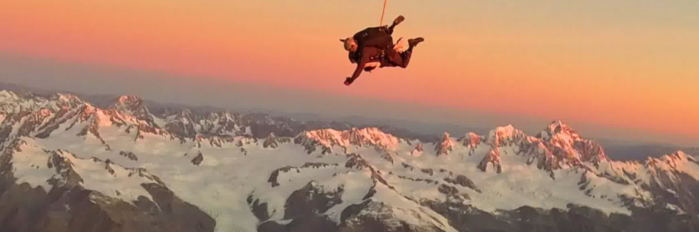 Skydiver above snowy mountains at sunset.