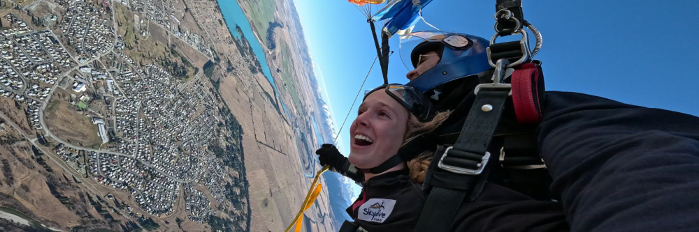 Two people tandem skydiving with view of landscape and small town below.