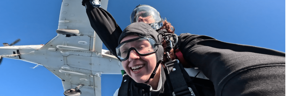 Two people tandem skydiving with airplane above.
