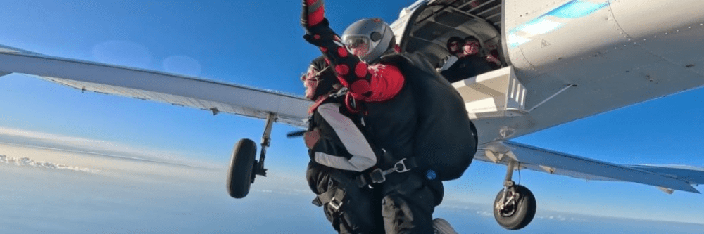 Two skydivers in tandem jumping from a plane under clear blue skies.