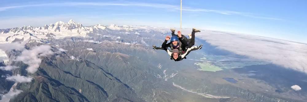 Two people tandem skydiving over mountains on a clear day.