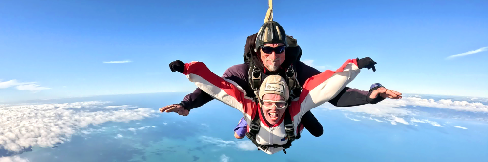 Two people tandem skydiving with ocean and clouds in the background.