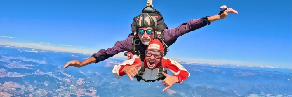 Two people skydiving with mountains visible below.
