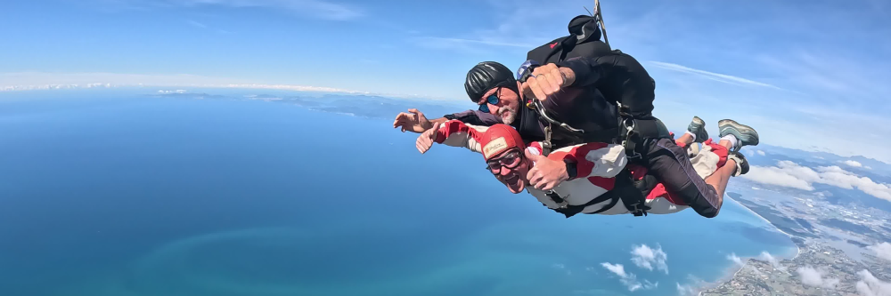 Two people tandem skydiving over the ocean with clear blue skies.