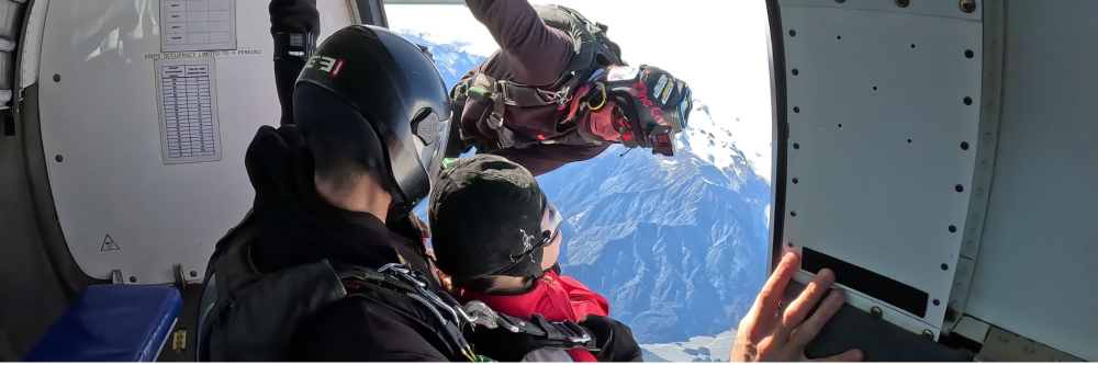 Skydivers preparing to jump from an airplane over mountains.