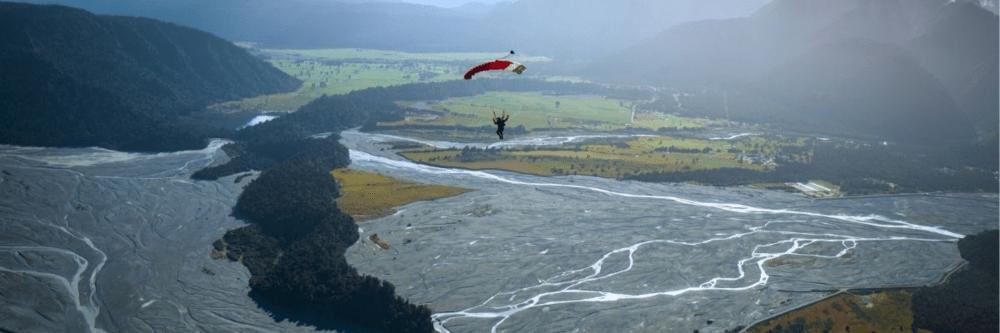 Skydiver with red parachute over a vast river delta landscape.