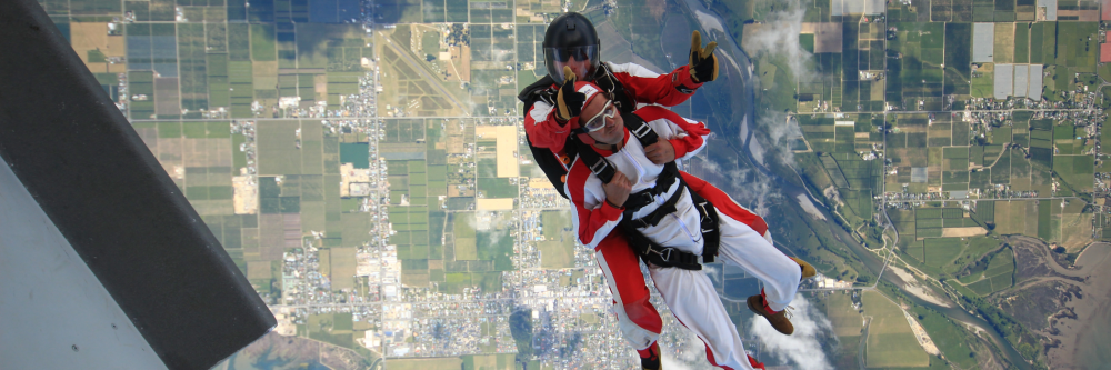 Tandem skydivers in mid-air with a landscape below.