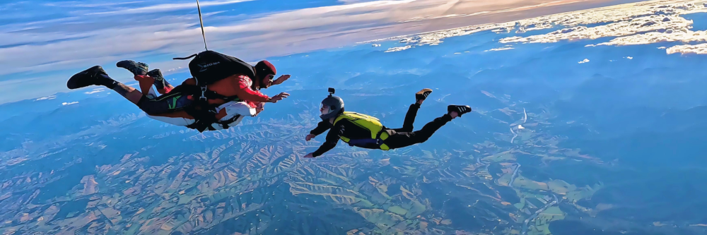 Three skydivers in mid-air over scenic landscape with mountains.